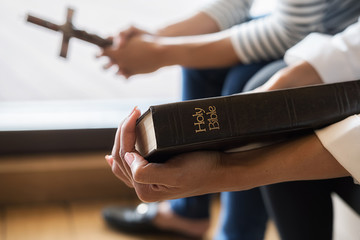 Obraz premium Christian woman praying with hands together on holy bible and wooden cross. Woman pray for god blessing to wishing have a better life and believe in goodness.