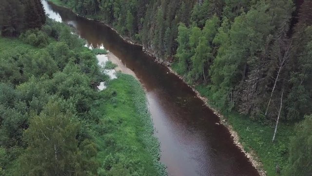 Beautiful Russian river located near the mixed forest, shrubs, flowers and trees against blue cloudy sky in summer day. Stock footage. Picturesque view from above of Russian nature