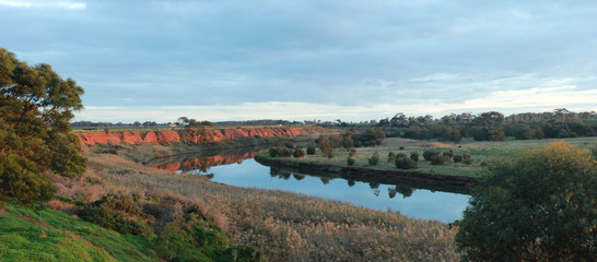 long stretching bend in a river that flows past red rock cliffs and into the ocean at Werribee south during golden hour, Victoria, Australia