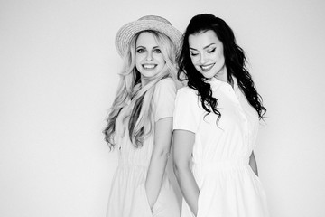 Brunette and blonde with bright dresses on a white background in a straw hat. Pink and yellow dress. Traveling with a mint suitcase. Black and white