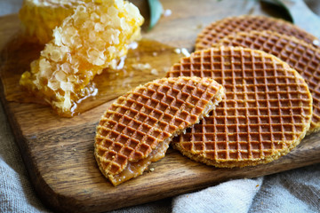 Traditional dutch Stroopwafels (honey wafers) on a wooden board with honeycombs next to them