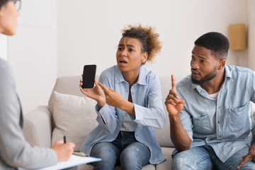 Emotional Afro Wife Showing Phone And Blaming Husband During Therapy