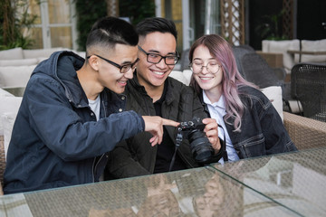 Three young hipsters sitting in a cafe and do photo.