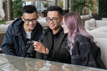 Three young hipsters sitting in a cafe and do photo.