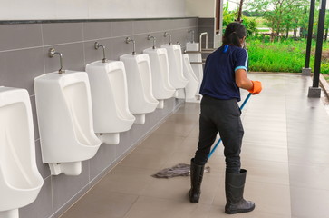 The young cleaner woman is cleaning by mopping the floor in toilet and the urinal in the public...