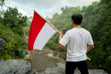 asian man with indonesian flag of indonesia on top of the mountain