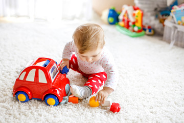Adorable cute beautiful little baby girl playing with educational wooden toys at home or nursery. Healthy happy toddler with colorful red car indoors. child learning colors and forms