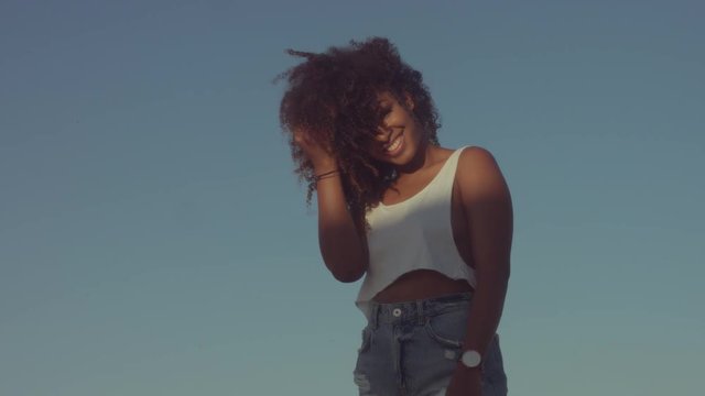 alone beauty mixed-race black woman with huge curly hair on sky background with a sunrise light Touches her curly hair and smiling to the camera