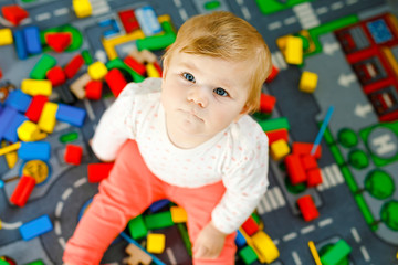 Obraz premium Adorable baby girl playing with educational toys . Happy healthy child having fun with colorful different wooden blocks at home in domestic room. Baby learning colors and forms