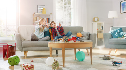 At Home: Cute Girl Playing in Video Game Console, Using Joystick Controller, Her Younger Brothe Cheers for Her. Happy Children Playing Videogames.
