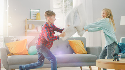 Adorable Little Boy and Sweet Little Girl Have a Pillow Fight in the Sunny Living Room. Siblings...
