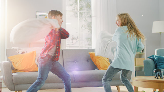 Adorable Little Boy and Sweet Little Girl Have a Pillow Fight in the Sunny Living Room. Siblings Having Fun Fighting with Pillows, Feathers Flying Around.