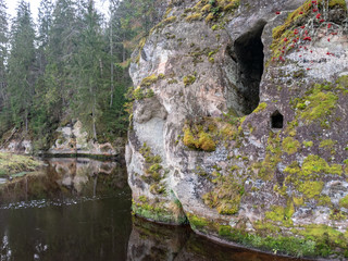 Sandstone rocks with caves reflect in dark water in Anfabrika, Ligatne, Latvia