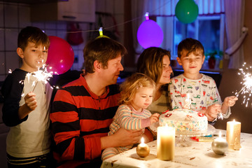 Adorable little toddler girl celebrating second birthday. Baby child, two kids boys brothers, mother and father together with cake and candles. Happy healthy family portrait with three children