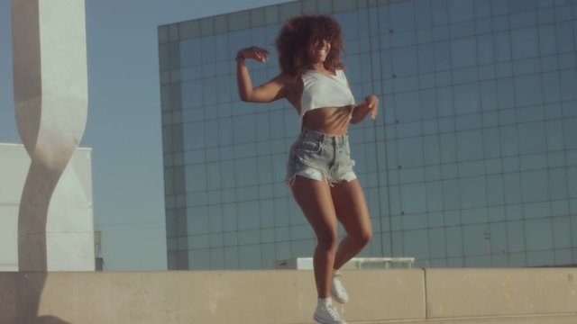 mixed race black young woman outdoors, summer sunset light, dancing rolling and shaking her huge afro hair, and jumping downstairs. Summer vibes