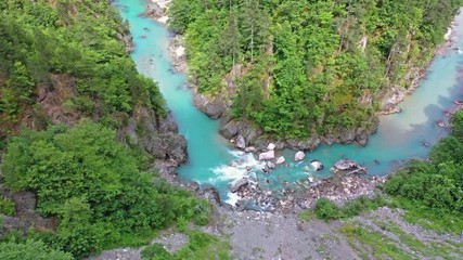 Flight of a quadcopter over a mountain's river canyon. We see the clear, transparent water of the river, it has the emerald color, the trees growing along the coast, and the mountains of northern Mont