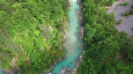 Flight of a quadcopter over a mountain's river canyon. We see the clear, transparent water of the river, it has the emerald color, the trees growing along the coast, and the mountains of northern Mont