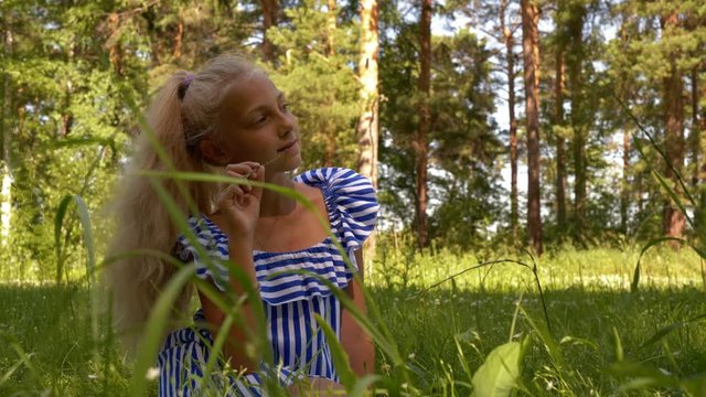 Free time in summer vacation. Thoughtful teen girl dreaming and thinking sitting on glade in nature park. Teenager waits her friends and eats grass. Walking outdoor in meadow. Carefree childhood.