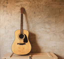 Acoustic guitar leans against the wall, on music instrument wooden box, shadow casting on concrete...