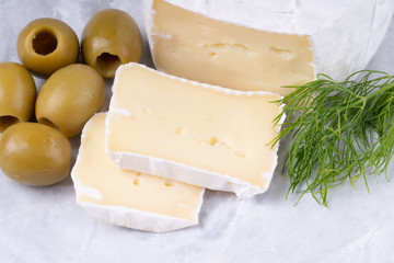 Sliced smelly camembert cheese with olives on a wooden rustic table