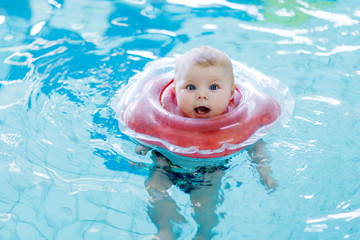 Cute little baby child learning to swim with swimming ring in an indoor pool