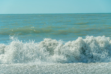 Close-up of sea wave with white foam comes ashore on a sunny day. Waves on the shore of the Black Sea on a sunny day
