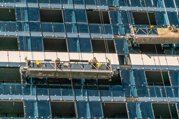 A group of workers in the cradle inspects the facade of a high-rise building. Glass building,...