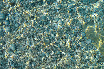 Fototapeta na wymiar Top view of blue, green and turquoise colors of water, surface of sea on rocks and bottom. Reflection of sun beams in water, shallow soil, shoal of ocean. Sea texture, background, pattern, wallpaper.