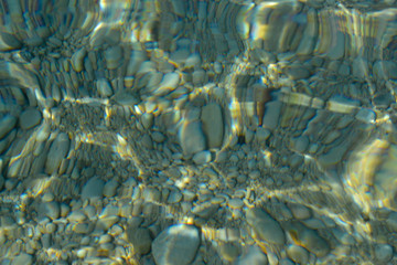 Top view of blue, green and turquoise colors of water, surface of sea on rocks and bottom. Reflection of sun beams in water, shallow soil, shoal of ocean. Sea texture, background, pattern, wallpaper.