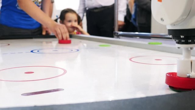 Air hockey table and person's hand playing with white robot arm. Media. Different working robots collection presented on the robotics forum exhibition