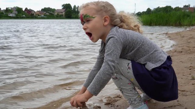 Playful girl 4 years old sit by a lake water and paying with sand. Gimbal motion