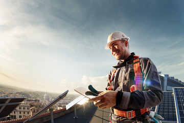 Solar energy engineer using tablet for check power station smiling in roof - obrazy, fototapety, plakaty
