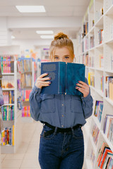 Young woman in book shop. Girl cover her face in bookstore.
