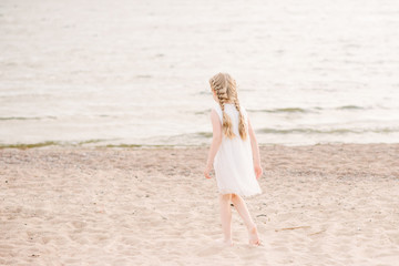 little girl in a white dress walks on the beach back