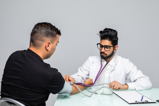 Indian Doctor holding dial while measuring man's blood pressure isolated on white background