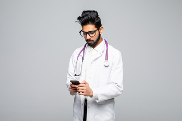 Indian male doctor looking at smartphone screen and sending text messages isolated on white background