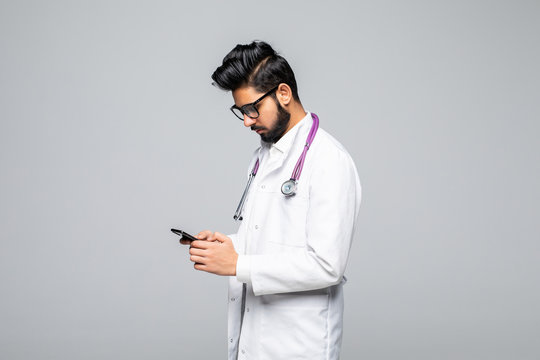 Indian male doctor looking at smartphone screen and sending text messages isolated on white background