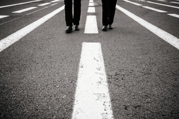 legs of two people in identical clotheswalking on the road black and white 