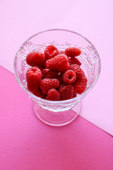Fresh, red raspberries in a crystal bowl isolated on coloured pink background with a geometric shape
