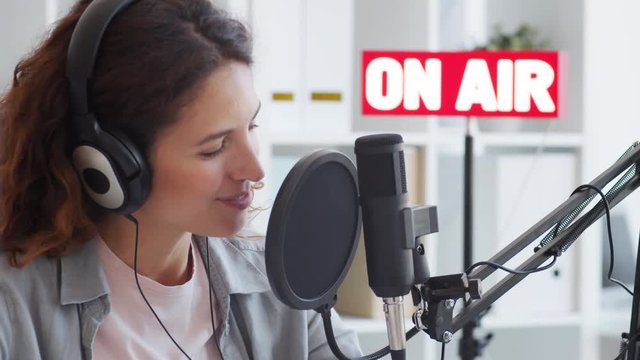 Close up of female Caucasian jockey with red curly hair sitting in broadcast studio, speaking into mike then taking off earphones, looking at camera with smile on face