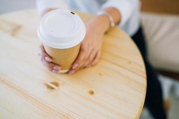 Female hands holding recyclable paper coffee cup at a cafe. Top view.