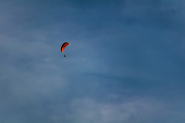 Paraglider on blue sky with orange parachute