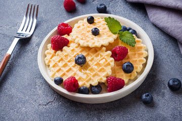 Corrugated waffle cookies with fresh raspberries and blueberries on a dark concrete background. Copy space.