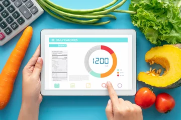 Foto op Plexiglas Calories counting , diet , food control and weight loss concept. woman using Calorie counter application on tablet at dining table with fresh vegetable and calculator © asiandelight