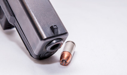 A black 9mm pistol muzzle with a single 9mm hollow point bullet next to it on a white background