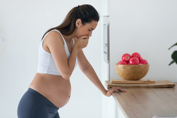 Disgusted pregnant young woman suffering with nausea in morning at home.