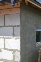 view of corner of house under construction, one wall of which is finished with base plaster layer, and second is not yet