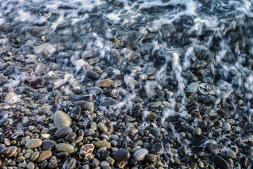 Landscape of stony beach. Wild stone beach with waves. The pebble stones are lying on the sea sand beach. Mystical background