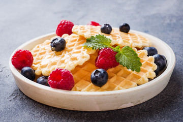 Corrugated waffle cookies with fresh raspberries and blueberries on a dark concrete background. Copy space.