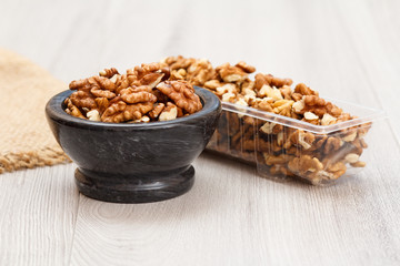 Walnuts in stone bowl and plastic container on a wooden background.